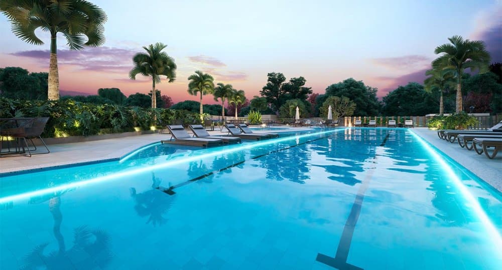 Piscina com raia e borda iluminada, espreguiçadeiras e palmeiras ao entardecer